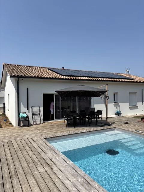 Maison de plain-pied équipée de panneaux photovoltaïques en toiture, avec terrasse en bois et piscine
